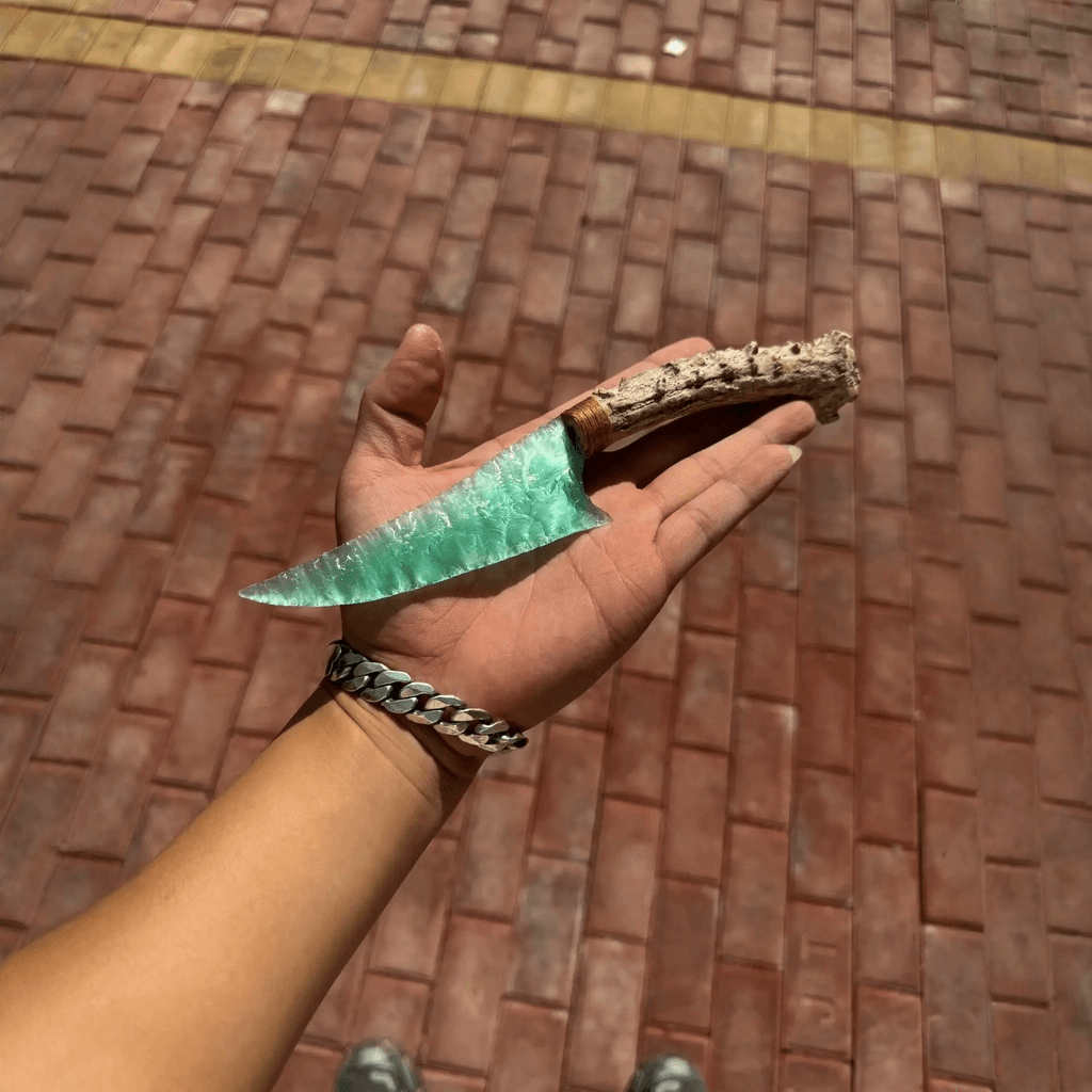 Hand holding seafoam-green stone blade dagger with antler handle outdoors