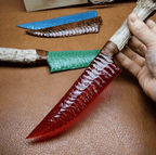 Stoneblade Forge red crystal dagger with antler handle held in hand, shown with blue and green blade variants on brown leather surface