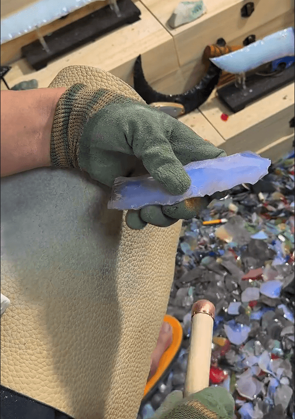 Stoneblade Forge hand-knapping process image—artisan wearing work gloves holds an opal-like stone slab while shaping it by flaking and knapping, showing real craftsmanship behind each stone blade’s scar patterns and sharp geometry.