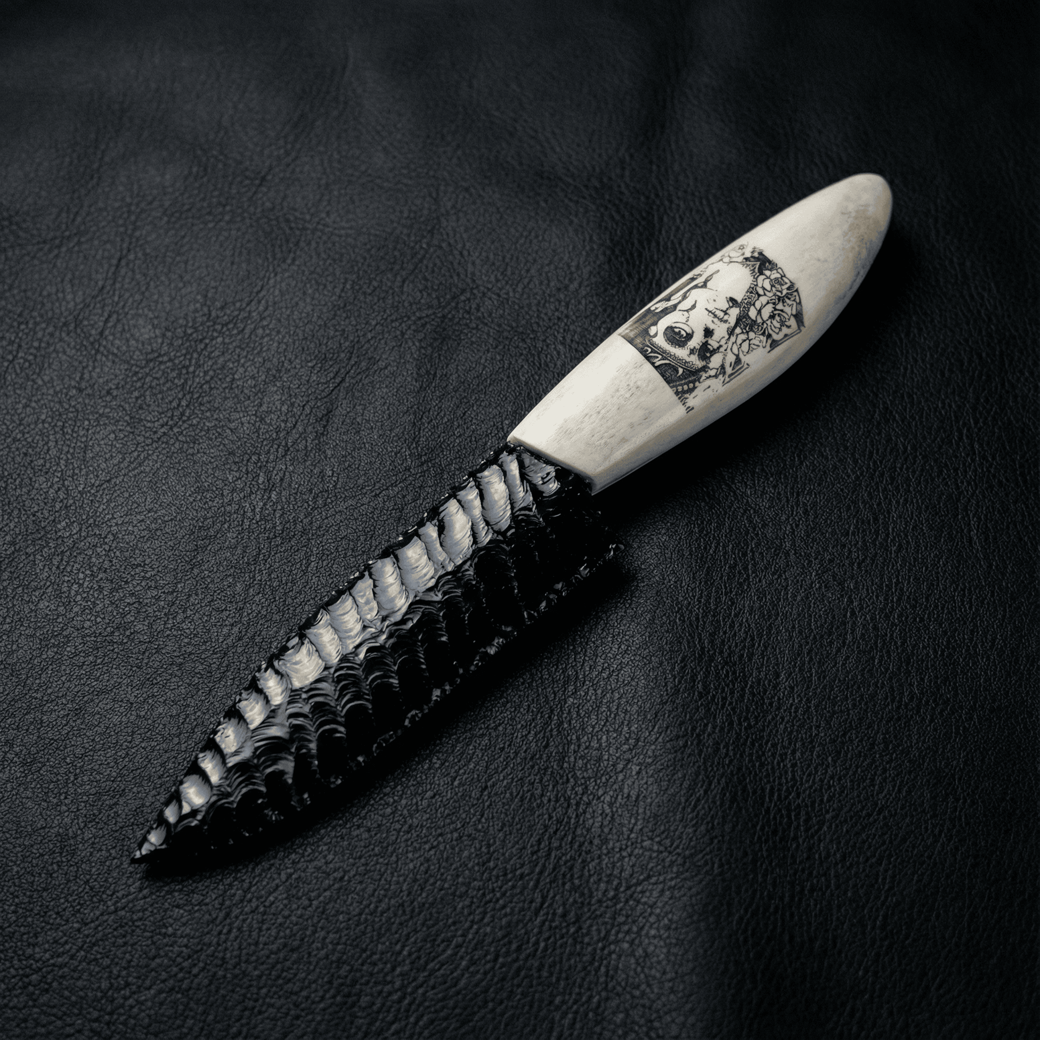 Stoneblade Forge Dagger Stone Blade “Grimwood” — black knapped-style dagger on black leather, featuring a bone-colored handle with skull artwork and glossy flake-scar texture.