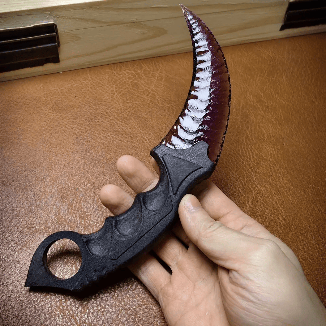 Deep purple crystal claw stone blade in hand on brown leather workbench, angled view