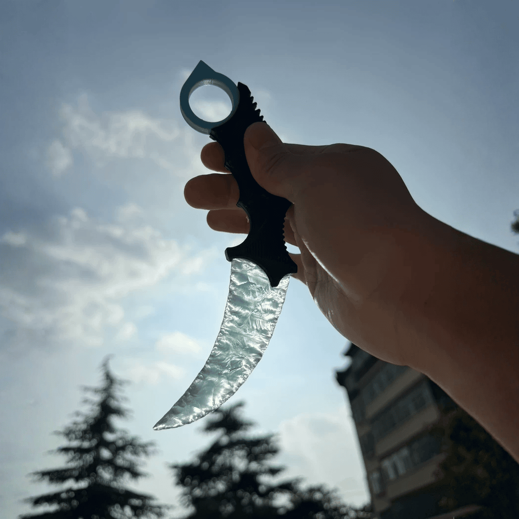 Hand holding ice-blue crystal claw stone blade against sky, silhouette view