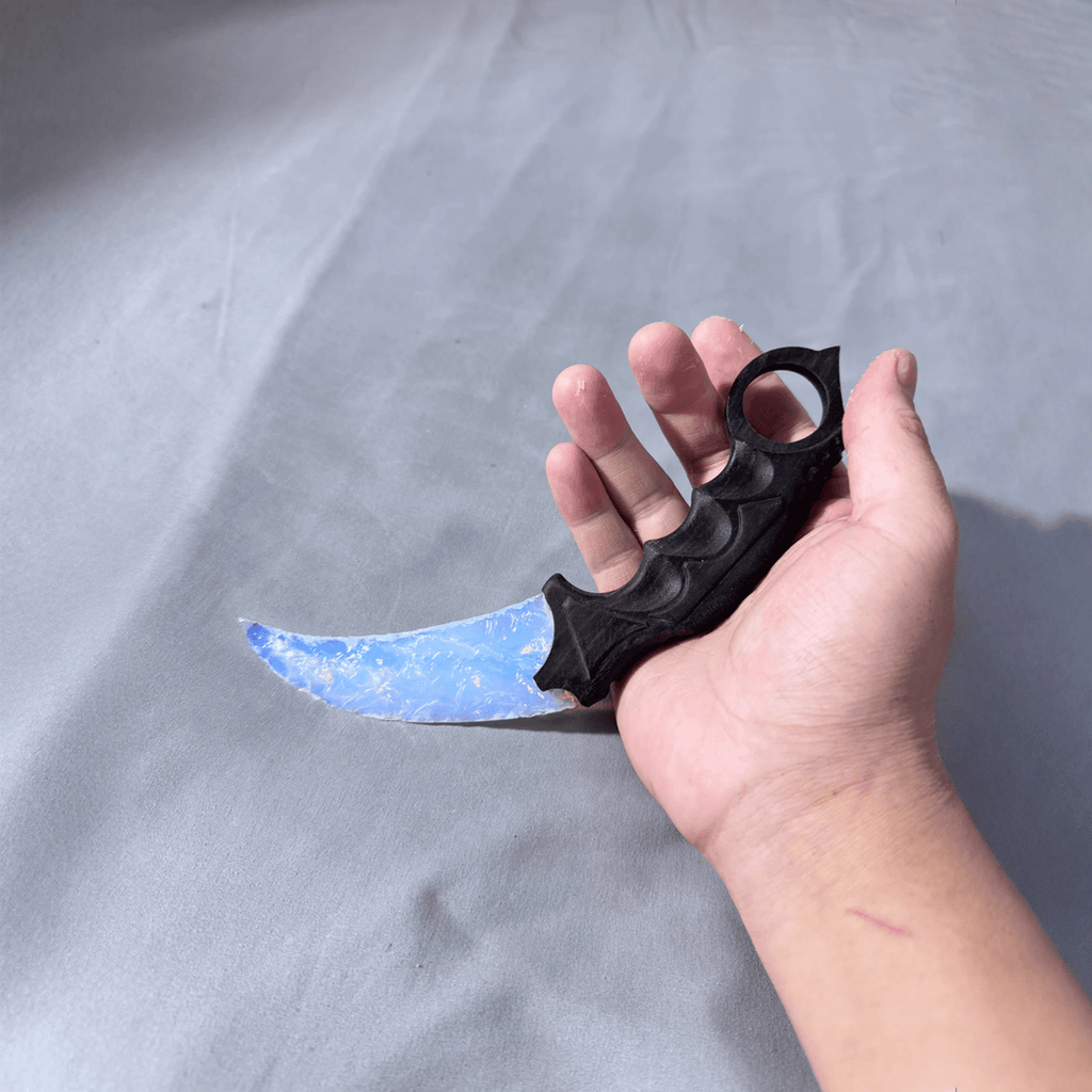 Opal-blue crystal claw stone blade in hand on grey surface, angled view