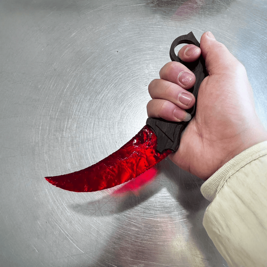 Red crystal claw stone blade with ring grip in hand on metal surface, angled view