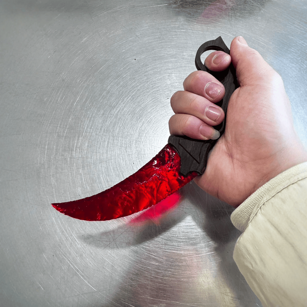 Red crystal claw stone blade with ring grip in hand on metal surface, angled view