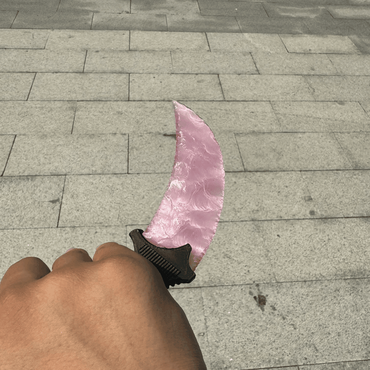 Pink crystal claw stone blade in hand with blade forward on stone pavement, angled view