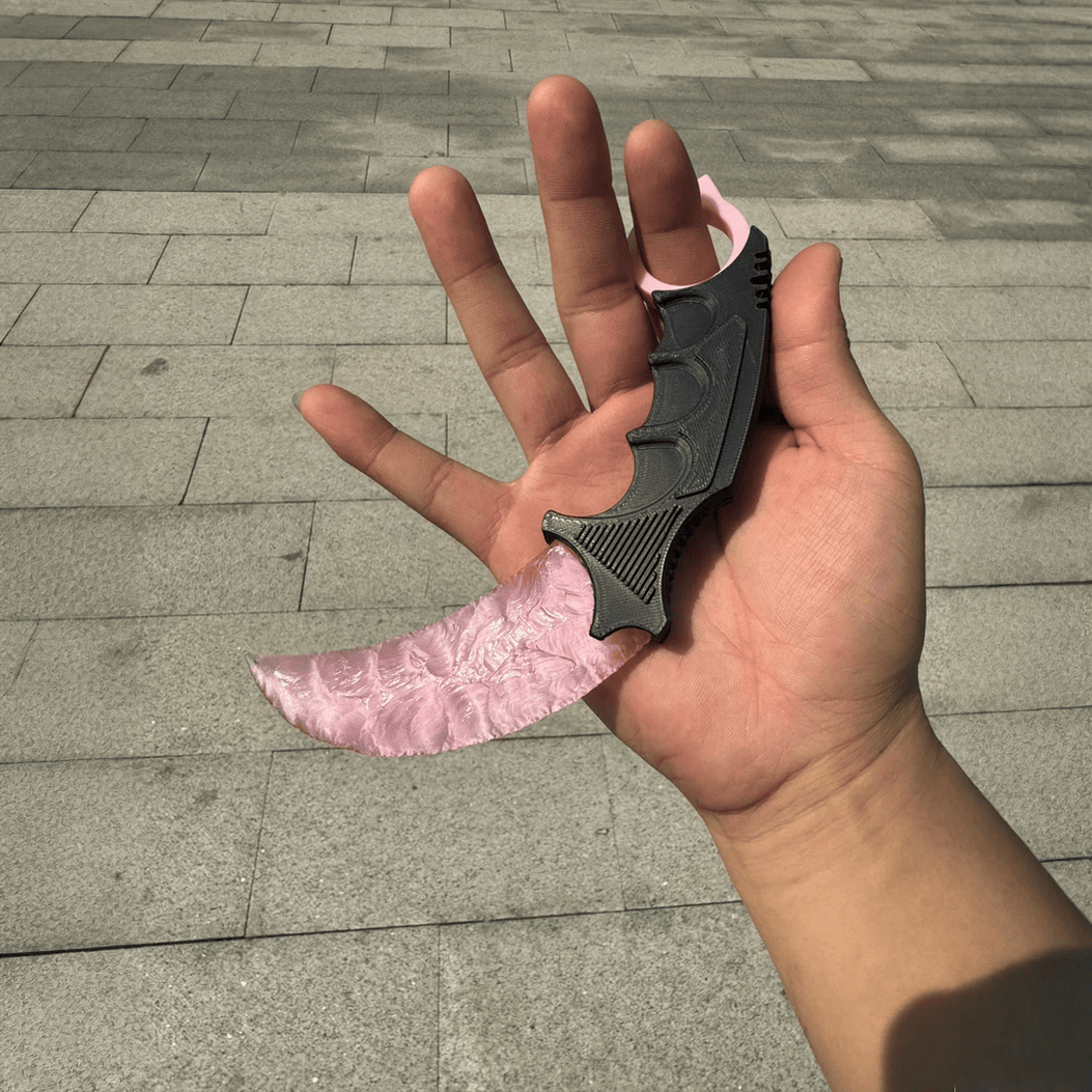 Hand holding pink crystal claw stone blade on stone pavement, full view