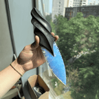 Handheld close-up showing the blue knapped-style blade paired with a black carved handle, shot near a window in daylight (Oblivion).