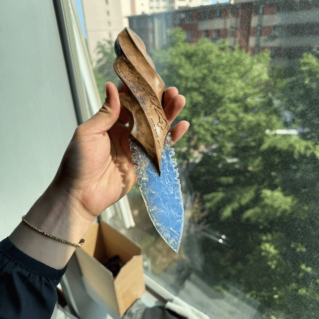 Handheld close-up of the blue knapped-style dagger with carved wood handle, photographed in natural window daylight (Oblivion).