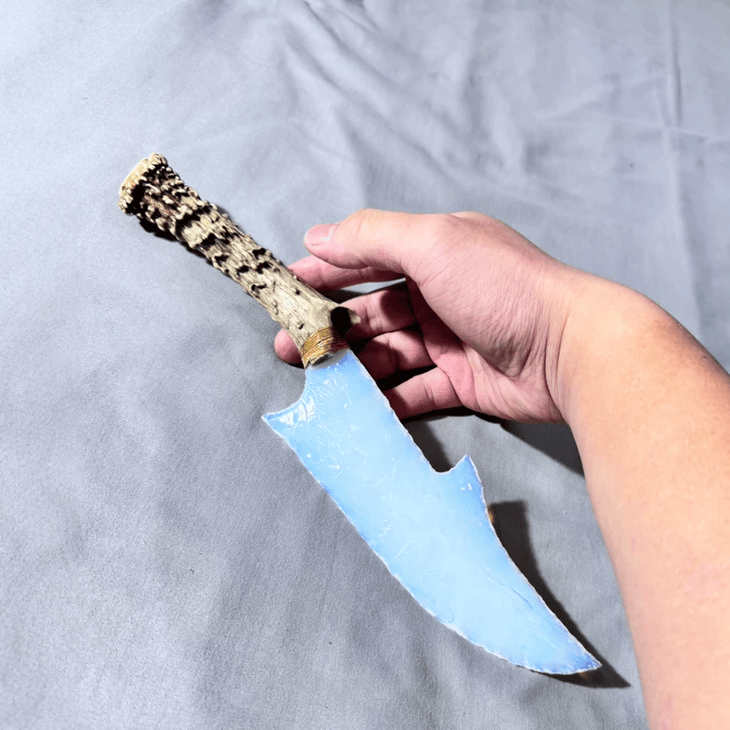 Stoneblade Forge Dagger Stone Blade “Ghostglass” — handheld icy-blue translucent blade with antler grip, shown on grey cloth backdrop.