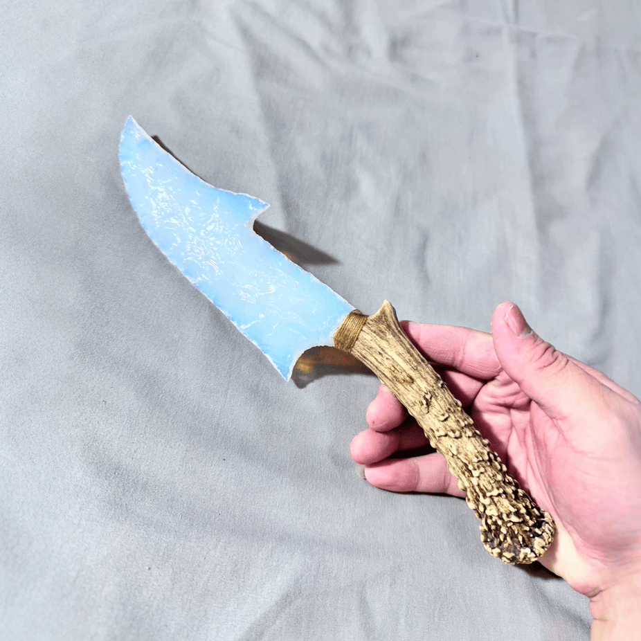 Stoneblade Forge Dagger Stone Blade “Ghostglass” — handheld close-up of the hooked knapped edge and antler-textured handle.