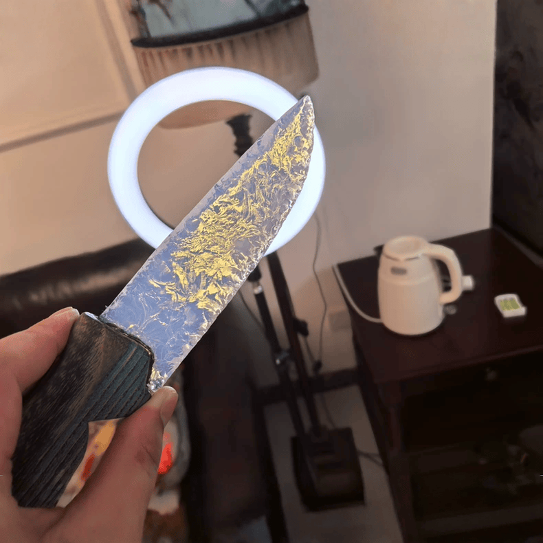 Close-up of the reflective Gildveil blade highlighting the gold-vein pattern, captured indoors with a ring light in the background.