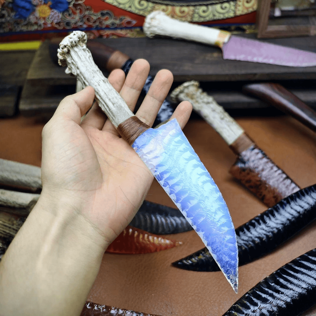 Stoneblade Forge Dagger Stone Blade “Moonwisp” — in-hand product shot highlighting the translucent blue blade texture and antler-style grip against a leather work surface.