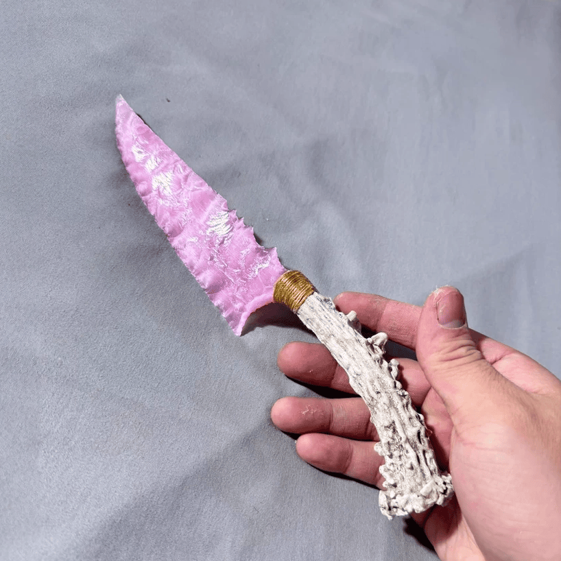 Rose-pink crystal stone blade dagger held in hand on grey fabric background