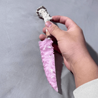 Rose-pink stone blade dagger held in hand with blade pointing downward on grey fabric