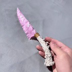 Close-up rose-pink stone blade dagger with antler handle and wrapped bolster in hand