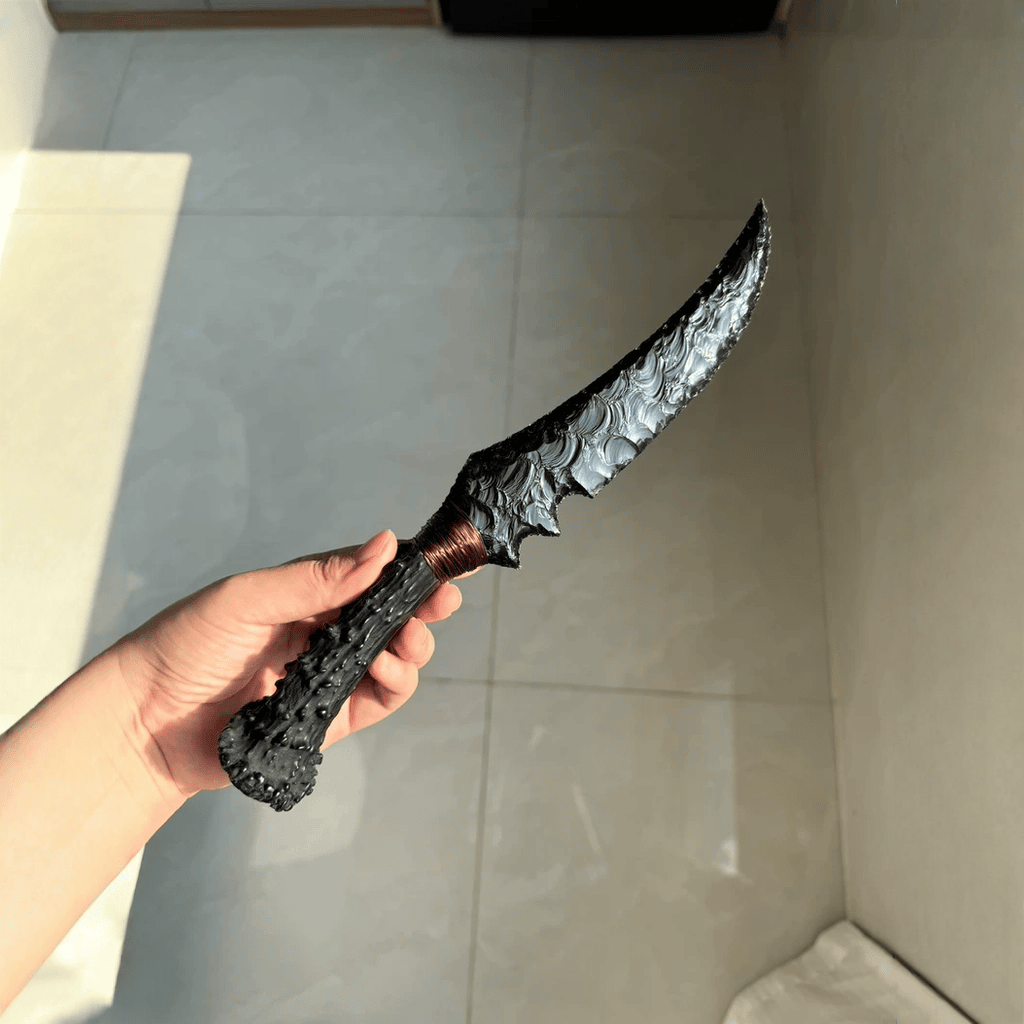 Handheld close-up of the Wraith dagger in sunlight, highlighting the curved edge profile, knapped surface texture, and copper-wrapped grip.