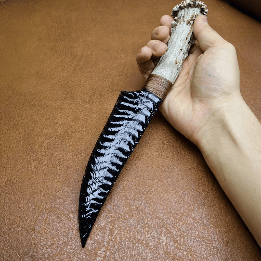 Hand holding Marauder obsidian crystal stone blade dagger, showing flaked blade texture and antler handle